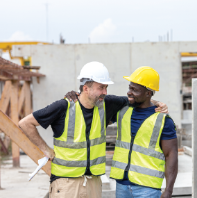 Two workers embracing in high vis tops and hard hats